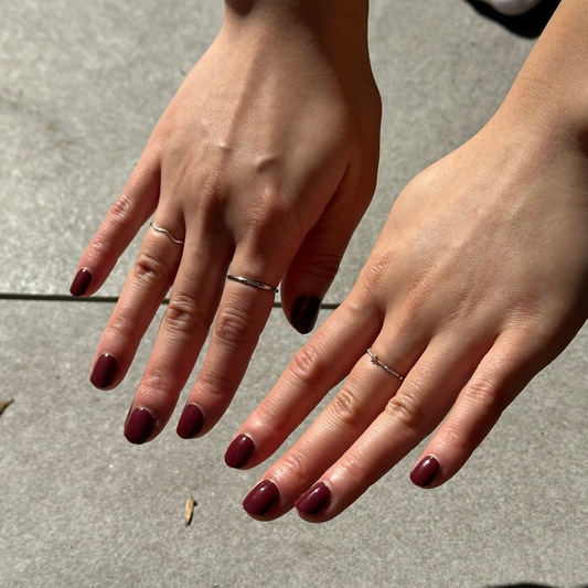 Close-up of two hands with red nail polish on a concrete surface