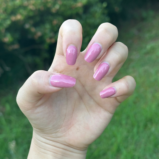 Hand with pink nail polish showing fingers against a grassy background