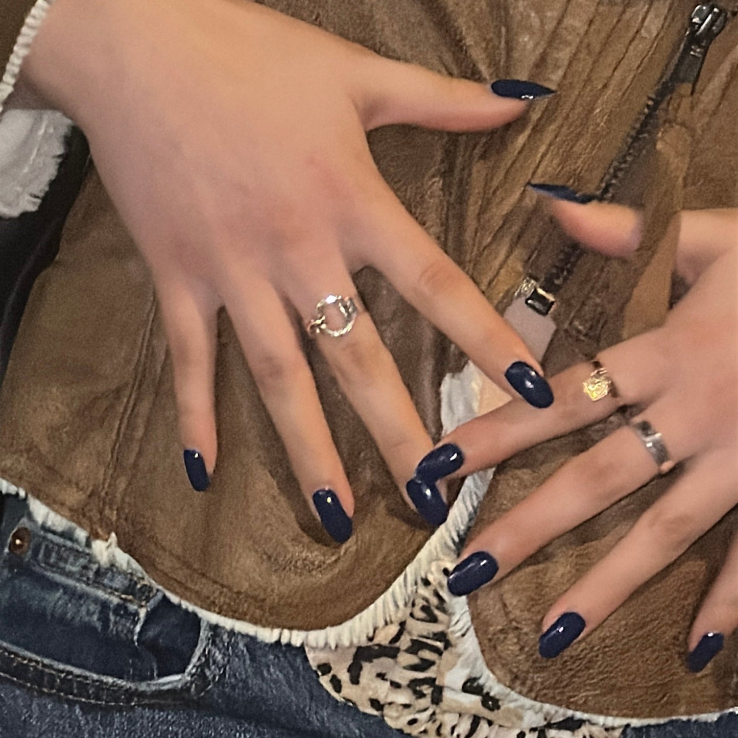 Close-up of hands with dark nail polish and rings on a textured fabric background