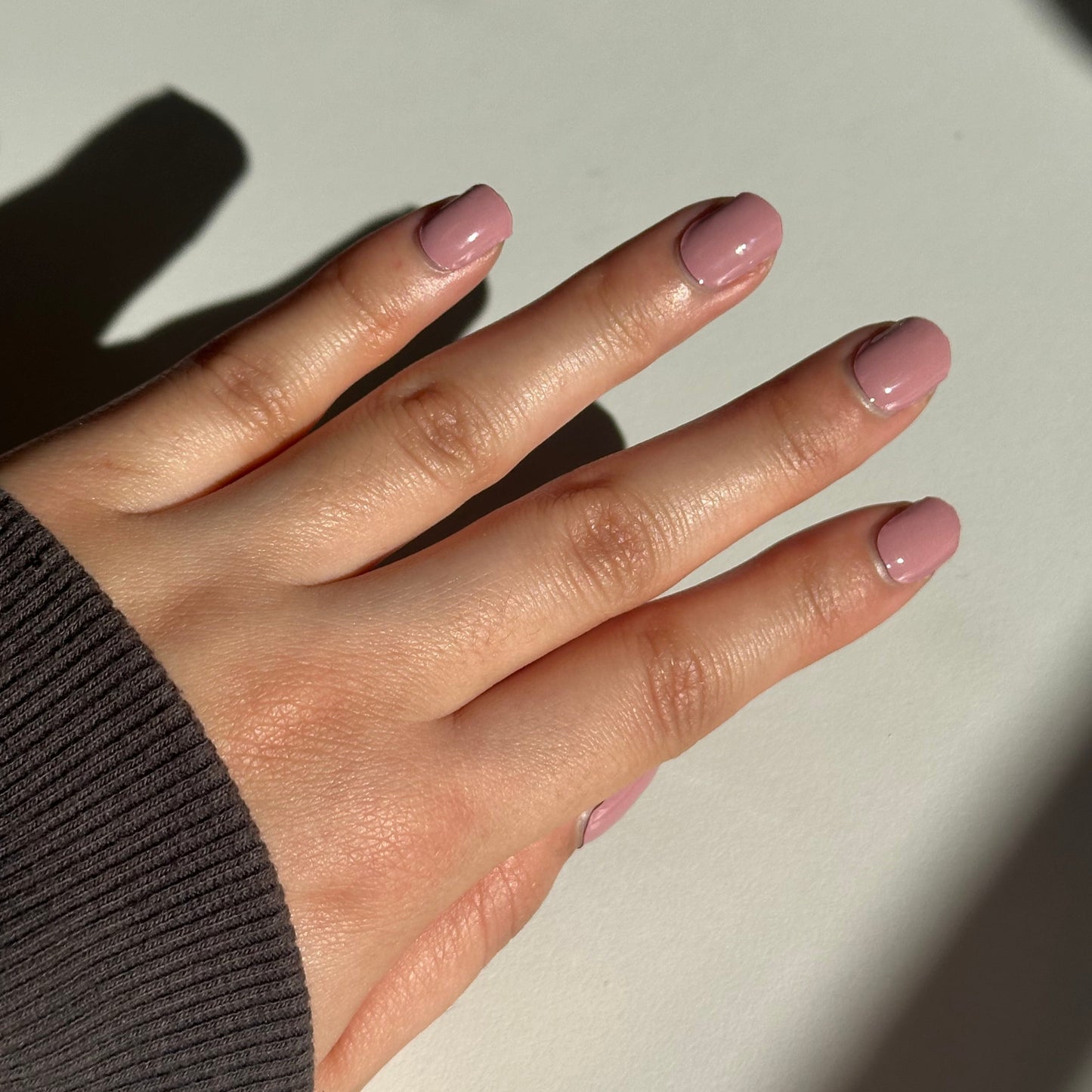 Hand with pink nail polish on a light background