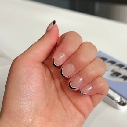 Hand with black and white nail design holding a phone with a blurred background