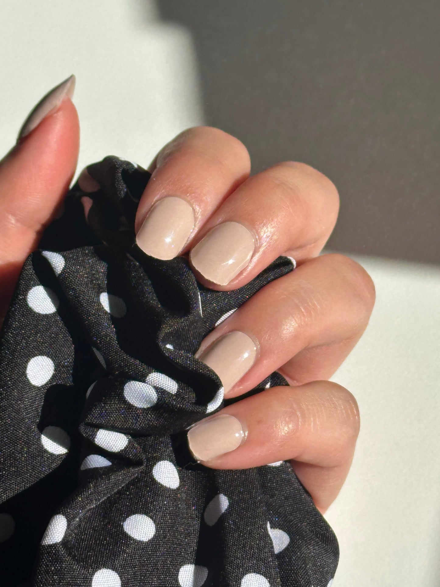 Hand holding a black scrunchie with white polka dots, close-up shot.