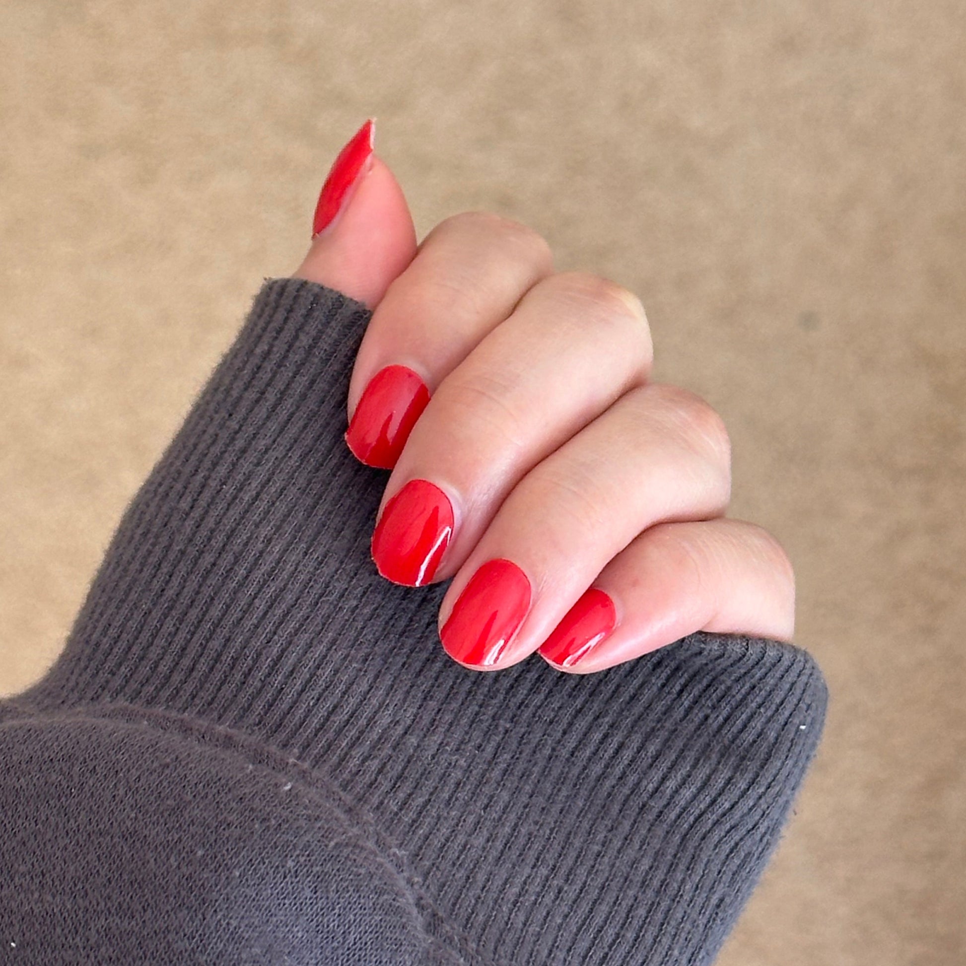 Hand with red nail polish wearing a dark gray sleeve against a beige background