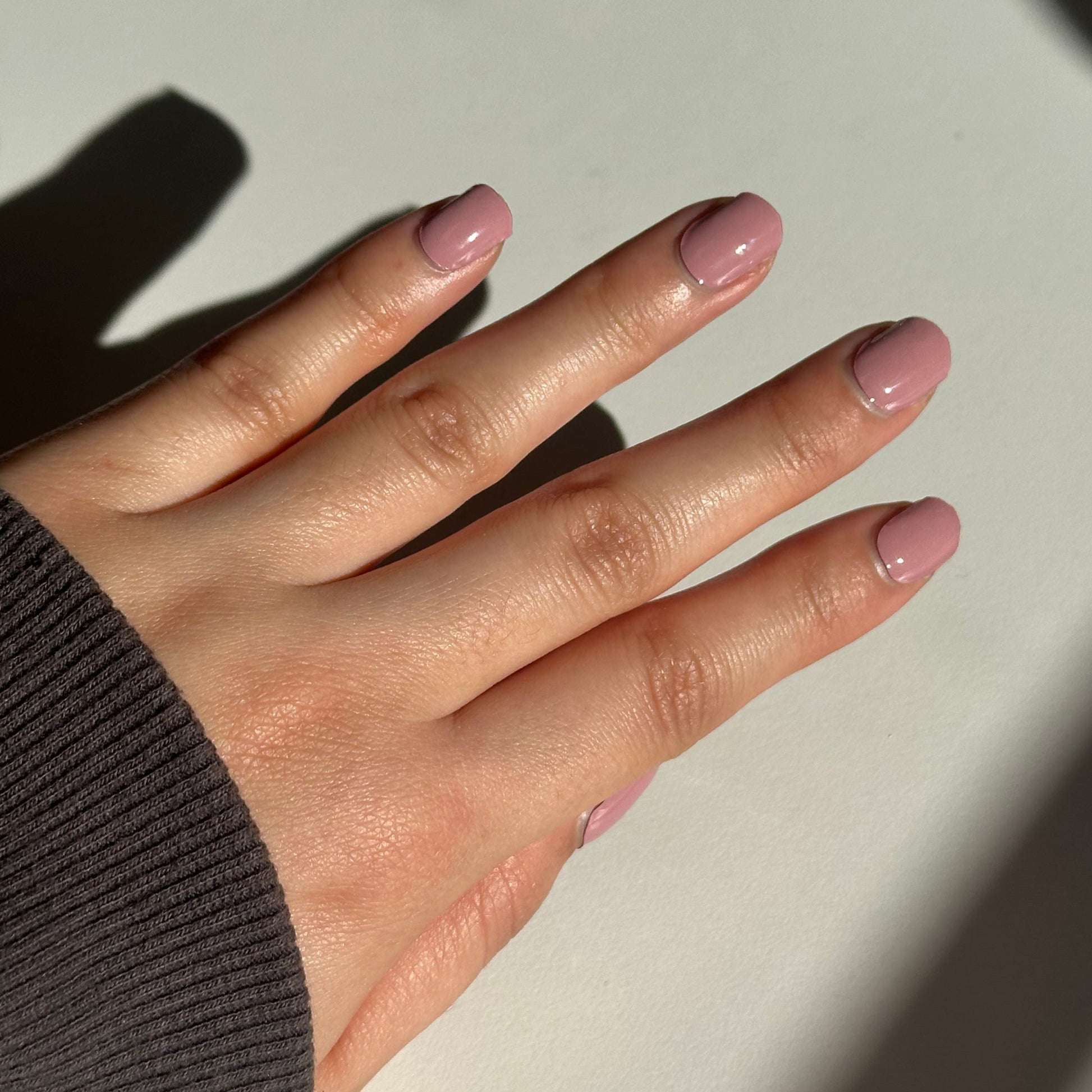 Hand with pink nail polish on a light background