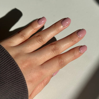 Hand with pink nail polish on a light background