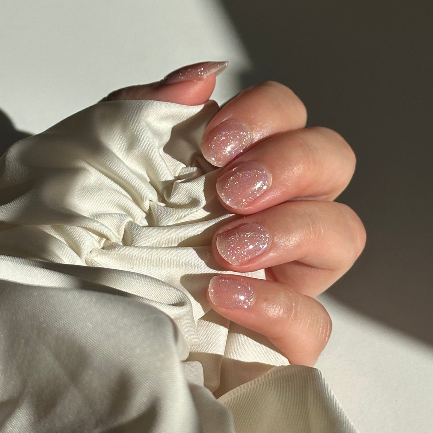 Close-up of a hand with glittery nail polish holding a white fabric garment.