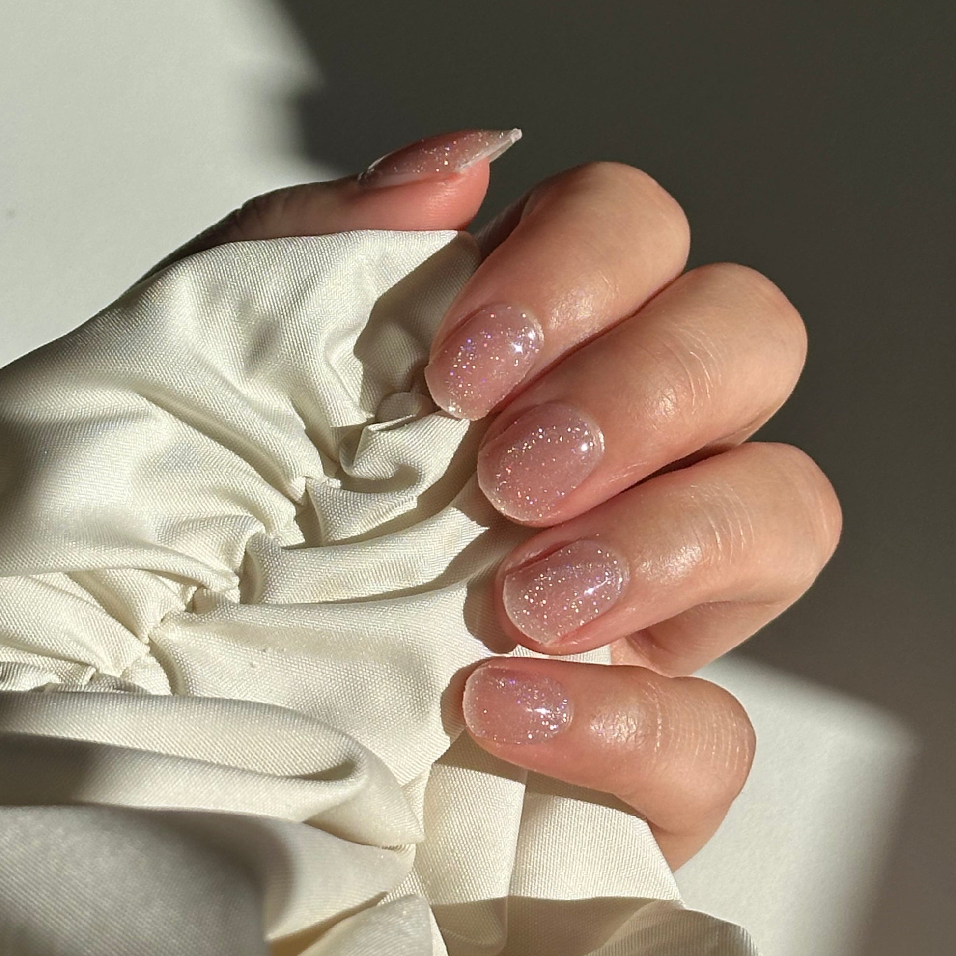 Close-up of a hand with pink nail polish holding a white fabric item.