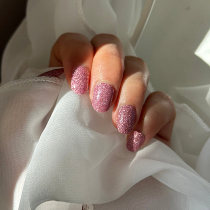 Hand with glittery pink nail polish holding white fabric
