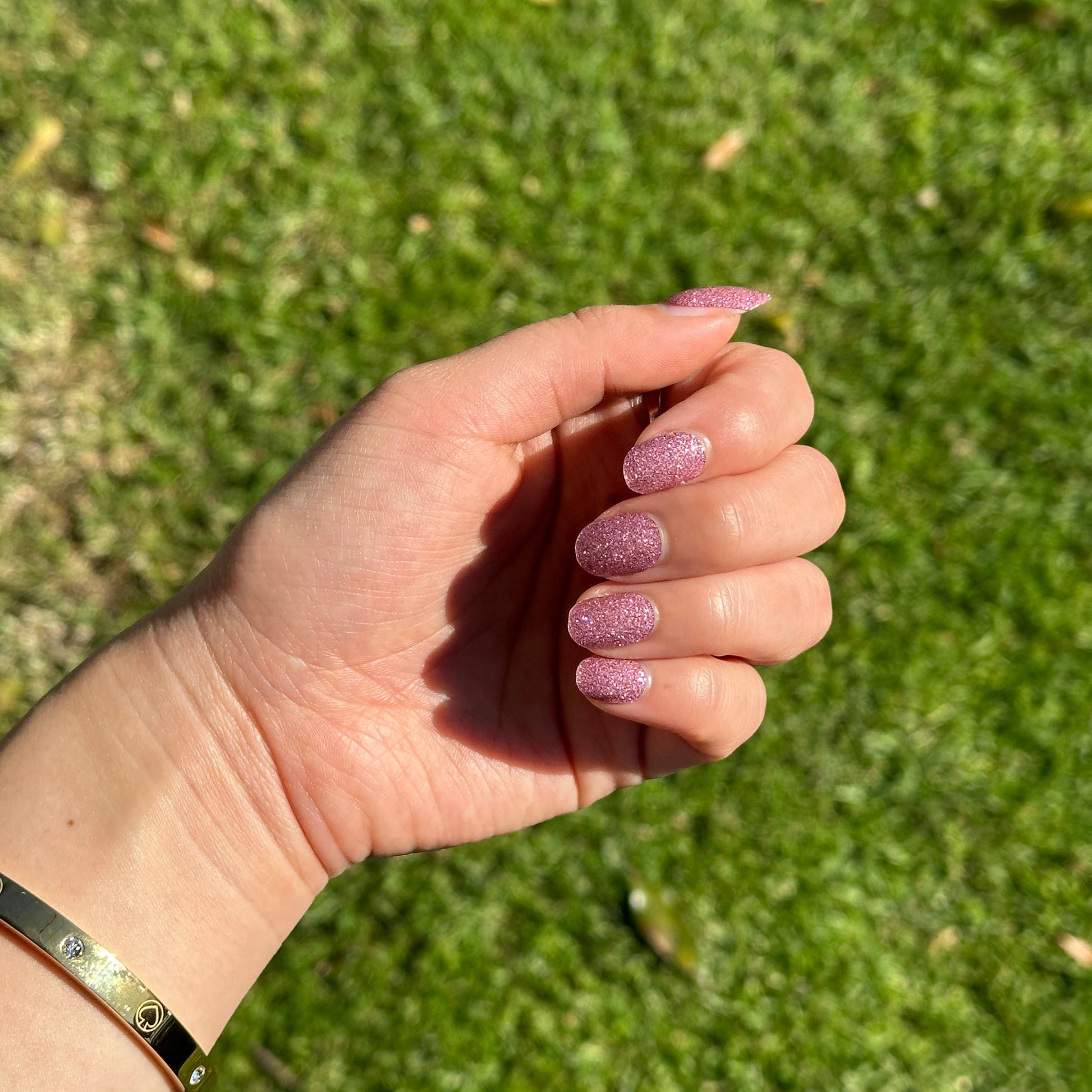 Hand with pink nail polish against a grassy background